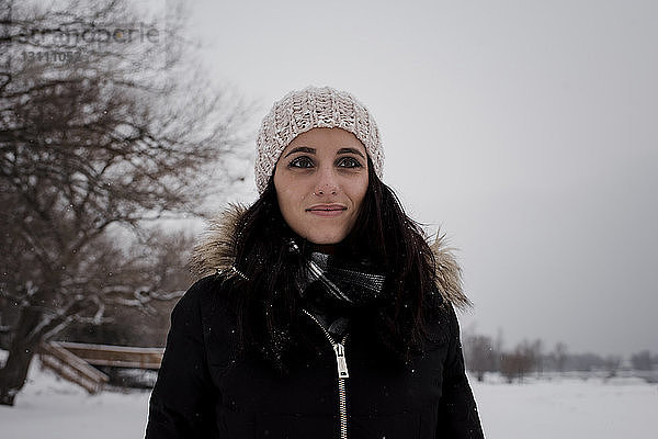 Lächelnde Frau schaut weg  während sie im Winter gegen den Himmel steht