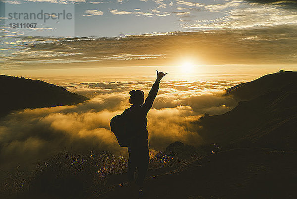 Silhouette einer Wanderin  die im Sonnenuntergang auf einem Berg stehend gestikuliert