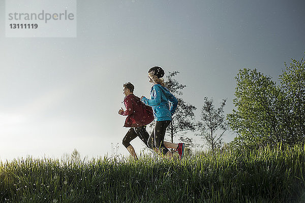 Seitenansicht von entschlossenen Athleten  die während des Sonnenuntergangs auf einem Rasenfeld laufen