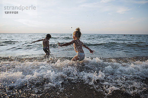 Verspielte Geschwister spielen in Wellen am Simcoe-See gegen den Himmel