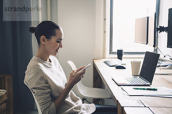 Geschäftsfrau benutzt Smartphone  während sie im Büro am Schreibtisch sitzt