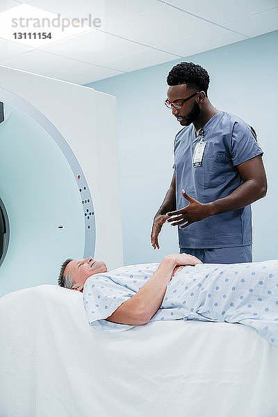 Arzt spricht mit Patient  der im Untersuchungsraum auf einem MRT-Scanner liegt