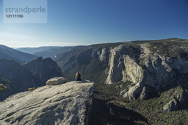Frau sitzt auf einer Klippe im Yosemite-Nationalpark vor blauem Himmel