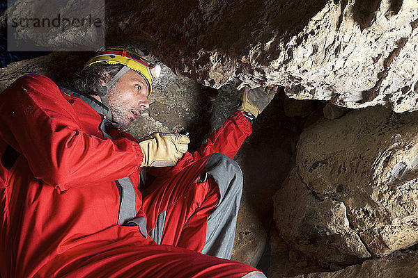 Niedrigwinkelansicht eines Archäologen  der in einer Höhle sitzend an Felsen arbeitet