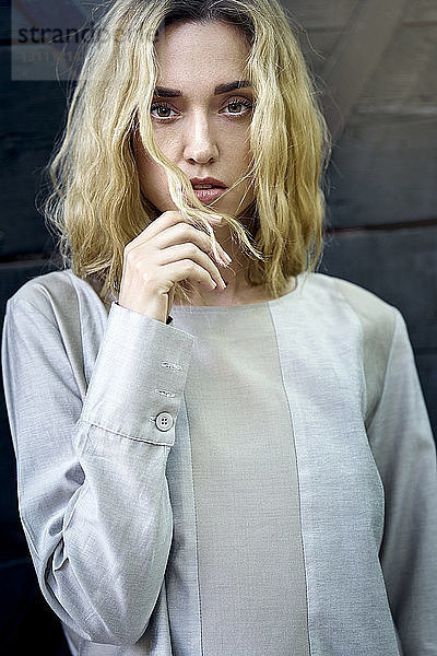 Porträt einer selbstbewussten jungen Frau mit blonden Haaren an der Wand stehend