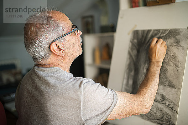 Konzentrierter älterer Mann  der zu Hause auf Leinwand skizziert