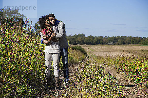 Paar umarmt sich auf grasbewachsenem Feld vor blauem Himmel