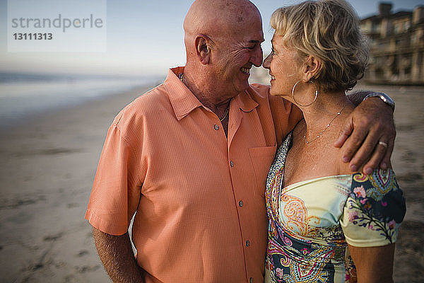 Lächelndes älteres Paar schaut sich an  während es am Meer gegen den Himmel steht