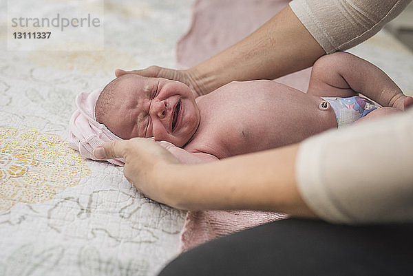 Abgehackte Hände einer Mutter  die weinende neugeborene Tochter auf dem Bett hält