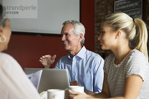 Lächelnder Geschäftsmann im Gespräch mit Kollegen während eines Treffens im Café