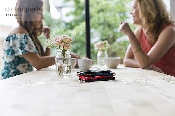 Freundinnen beim gemeinsamen Kaffeetrinken im Café mit Smartphones auf dem Tisch