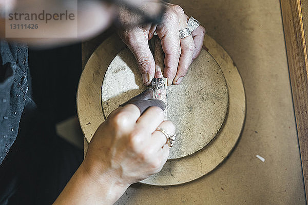 Hochwinkelansicht einer Kunsthandwerkerin  die in einer Werkstatt Schmuck auf dem Tisch herstellt