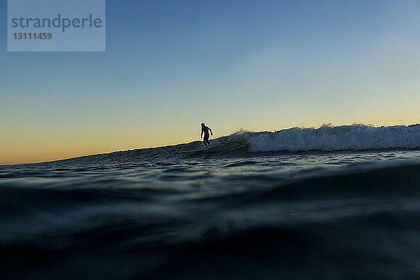 Fernansicht eines Mannes mit Silhouette  der bei Sonnenuntergang auf dem Meer surft