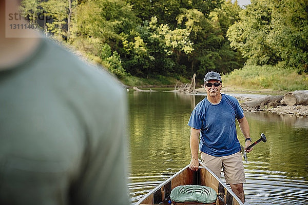 Mann mit Sonnenbrille steht mit Freund am Seeufer am Boot