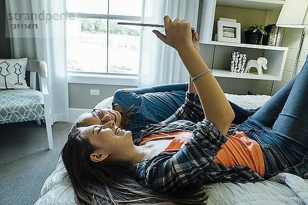 Glückliche Schwestern  die zu Hause im Bett liegend einen Tablet-Computer benutzen