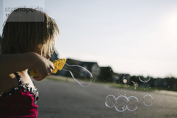 Seitenansicht eines Mädchens  das auf einem Spielplatz gegen den klaren Himmel einen Blasrohr-Stab bläst
