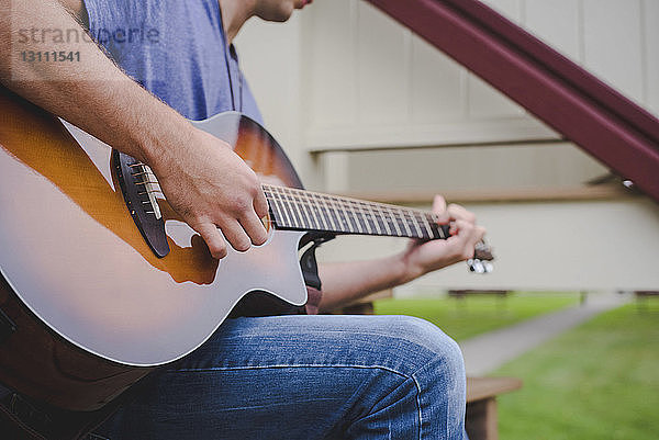 Ein Mann spielt Gitarre  während er auf einer Parkbank sitzt