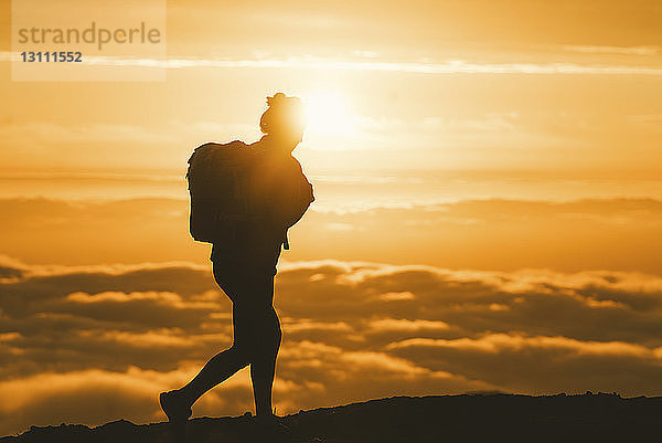 Silhouette einer Wanderin  die bei Sonnenuntergang auf einem Berg wandert