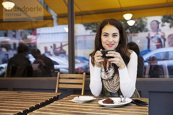 Porträt einer Frau  die eine Kaffeetasse hält  während sie in einem Straßencafé sitzt