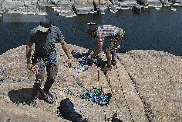 Hochwinkelaufnahme von Freunden  die bei Sonnenschein Kletterseile an einer Felsformation über dem See befestigen