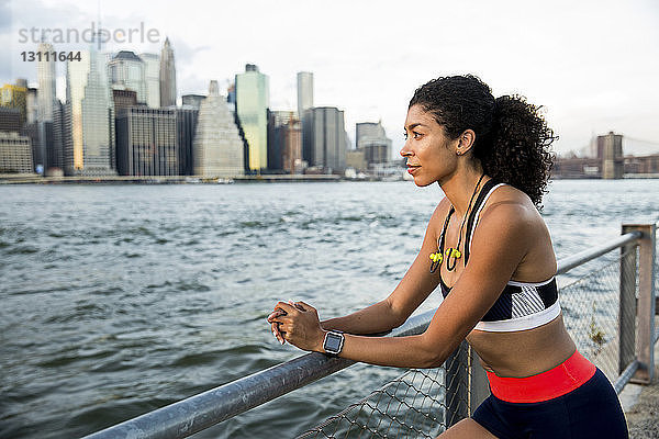 Nachdenkliche Sportlerin steht am Fluss gegen den Himmel in der Stadt