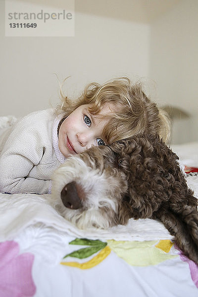 Porträt eines glücklichen Mädchens  das sich mit seinem Hund zu Hause im Bett ausruht