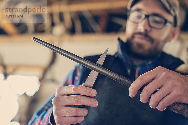 Niedriger Blickwinkel eines männlichen Präparators beim Schärfen von Messern in einem Workshop