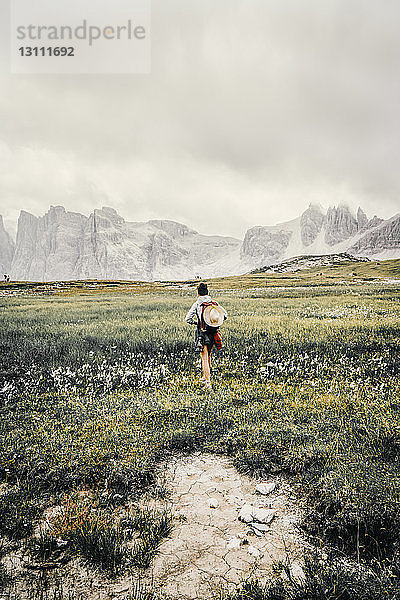 Rückansicht einer Wanderin mit Rucksack  die auf einem Grasfeld vor bewölktem Himmel steht