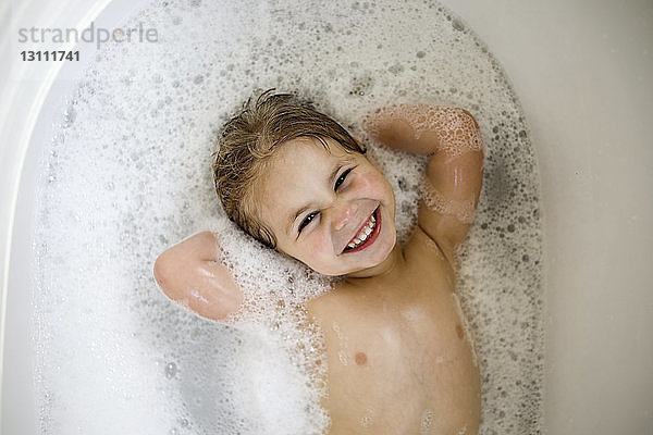 Überkopf-Porträt eines fröhlichen Mädchens mit Händen hinter dem Kopf in der Badewanne liegend
