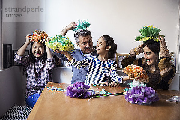 Fröhliche Familie spielt mit selbstgemachten Papierblumen  während sie am Tisch sitzt