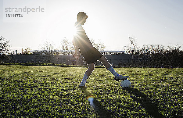 Mann übt Fußball auf Grasfeld gegen klaren Himmel bei Sonnenuntergang