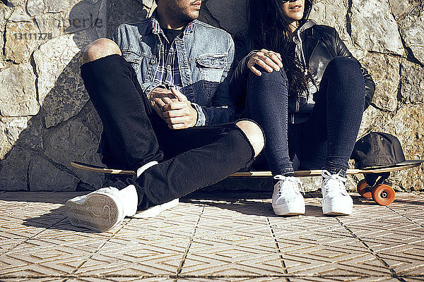 Niedriger Teil des Paares sitzt auf einem Skateboard gegen eine Steinmauer