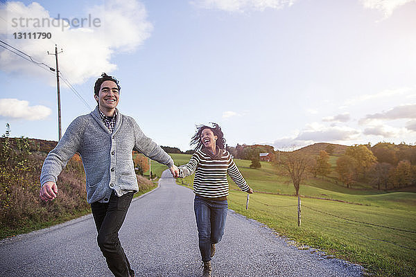 Fröhliches Paar rennt auf Fußweg gegen den Himmel