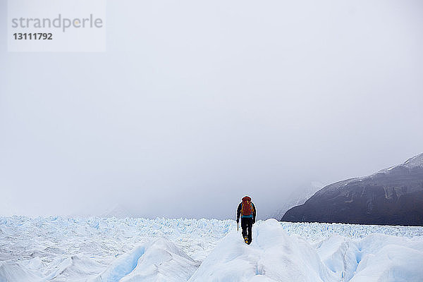 Rückansicht eines Mannes  der auf einem schneebedeckten Feld gegen den Himmel läuft