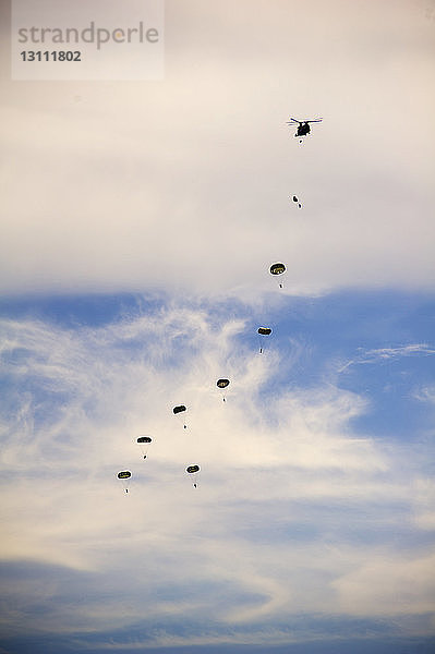 Tiefwinkelansicht von Fallschirmjägern  die während einer Flugschau am bewölkten Himmel fliegen