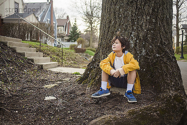 Nachdenklicher Junge schaut weg  während er am Baumstamm sitzt