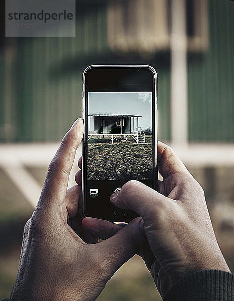 Ausgeschnittene Hände eines Mannes  der mit einem Mobiltelefon ein Haus fotografiert