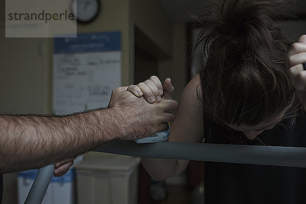 Abgehackte Hand eines Mannes tröstet schmerzhafte schwangere Frau auf der Krankenhausstation