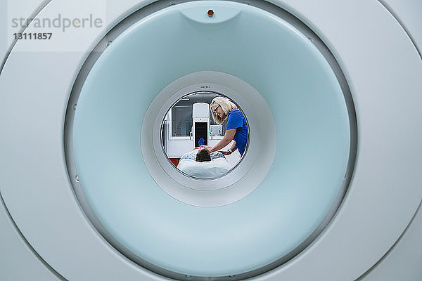 Krankenschwester bereitet Patient für MRT-Scan im Krankenhaus vor  der durch den Scanner gesehen wird