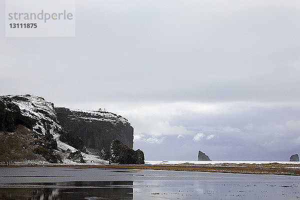 Landschaftliche Ansicht von Dyrholaey Island vor bewölktem Himmel im Winter