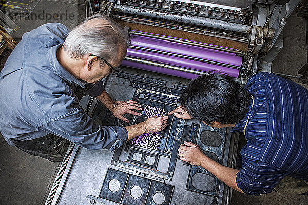 Schrägansicht von Arbeitern  die in der Werkstatt den Buchdruck an Maschinen reparieren