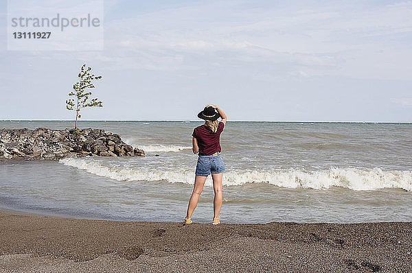 Rückansicht einer Frau mit Hut  die am Strand gegen den Himmel steht