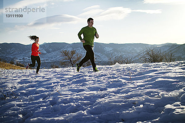 Paar joggt auf Schneefeld gegen den Himmel