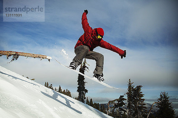 Männlicher Snowboarder springt auf schneebedecktem Berg gegen den Himmel