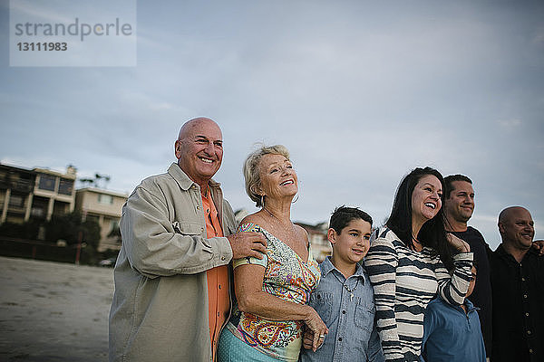 Glückliche Familie steht bei Sonnenuntergang am Strand gegen den Himmel