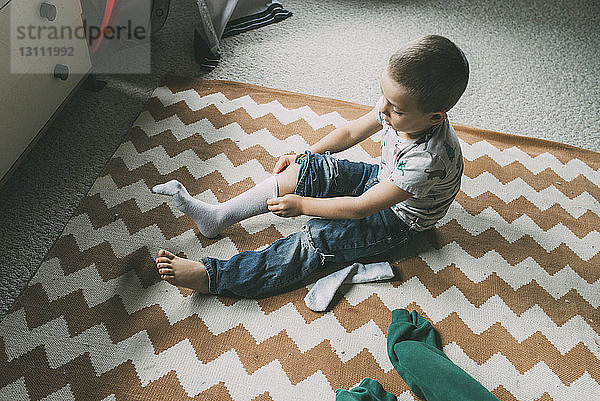 Schrägansicht eines Jungen  der zu Hause auf dem Teppich sitzend an einer Socke zieht