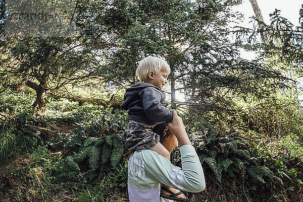 Seitenansicht eines Mädchens  das einen Bruder auf den Schultern trägt  während es an Bäumen steht