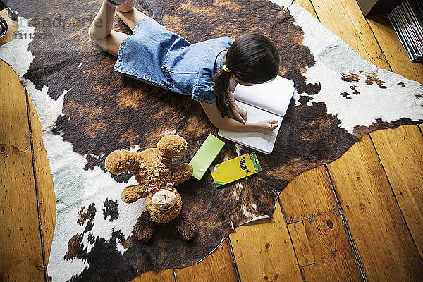 Hochwinkelaufnahme eines Mädchens  das auf einem Teppich liegt und zu Hause studiert