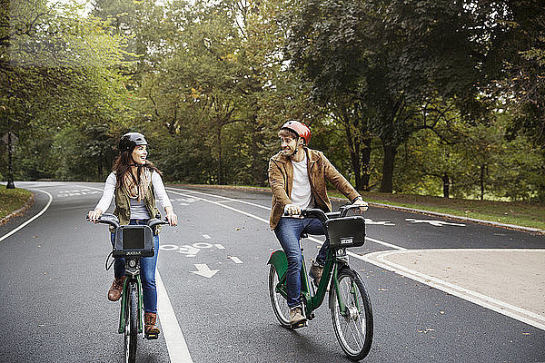 Lächelndes Paar beim Fahrradfahren auf der Straße im Park