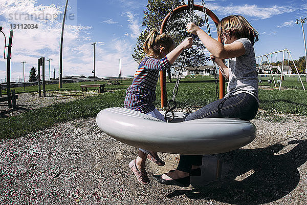 Schwestern spielen bei Sonnenschein auf der Schaukel auf dem Spielplatz